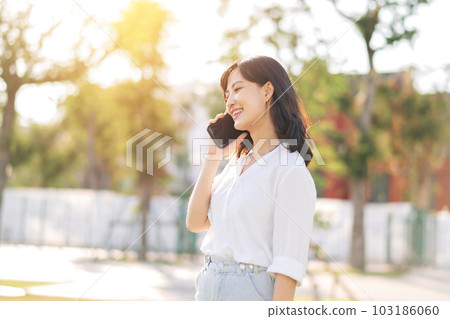 Portrait beautiful young asian woman with smart mobile phone around outdoor nature view in a sunny summer day 103186060