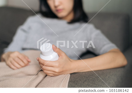 Asian woman with cold and flu reading instructions on medicine bottle 103186142