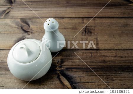 Sugar bowl and salt shaker on a wooden table. 103186331