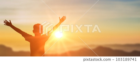 Boy raising hands over sunset sky, enjoying life and nature. Happy Kid in mountains looking on sun. Silhouette of child in sunlight rays. copy space 103189741