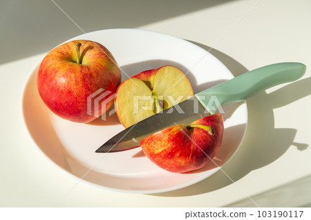 Ripe red apples in plate with a knife. Cut an Apple before eating to follow diet or fasting days Ripe red apples in plate with a knife. Cut an Apple before eating to follow diet or fasting days 103190117