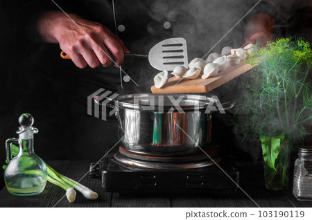 The chef cooks dumplings in a saucepan in the restaurant kitchen. Close-up of the hands of the cook during work The chef cooks dumplings in a saucepan in the restaurant kitchen. Close-up of the hands of the cook during work 103190119
