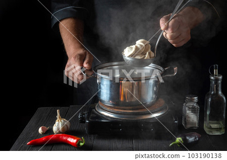 Professional chef cooks meat dumplings in a saucepan in the restaurant kitchen. Close-up of the hands of the cook during work. Free advertising space. Professional chef cooks meat dumplings in a saucepan in the restaurant kitchen. Close-up of the hands of the cook during work. Free advertising space. 103190138