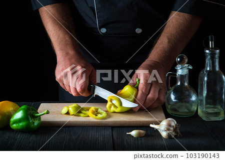 The chef is cutting bell peppers for salad in the restaurant kitchen. Close-up of a cook hands while working. Free advertising space 103190143