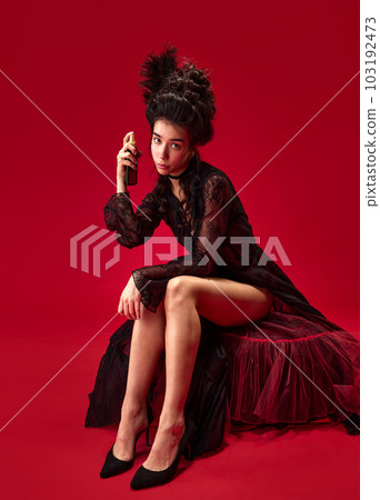 Portrait of beautiful, elegant, tender young girl doing makeup, applying toner, sunscreen on face against red background 103192473