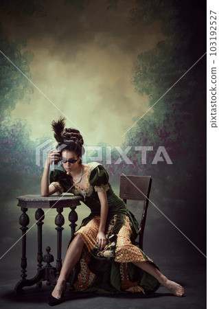 Hangover. Portrait of young girl, royal person in elegant dress sitting at table and leaning beer mug to head against dark vintage background Hangover. Portrait of young girl, royal person in elegant dress sitting at table and leaning beer mug to head against dark vintage background 103192527