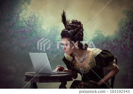 Misunderstanding. Young beautiful woman, royal person in elegant dress looking on laptop with funny face against dark vintage background 103192543