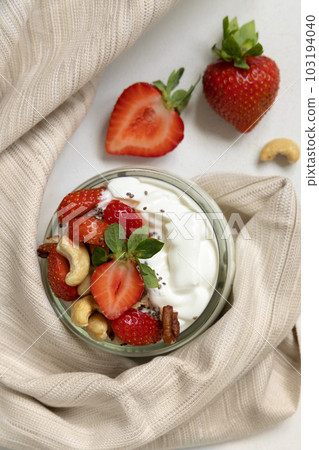 Greek yogurt, nuts and strawberries in a glass jar on a white table top view 103194040