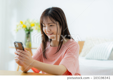 一個女人在客廳裡看著她的智能手機 一個女人在客廳裡看著她的智能手機 103196341