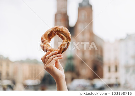 Tourist is holding prezel, traditional polish snack on the Market square in Krakow. Traveling Europe in spring. Food banner 103198716