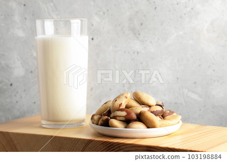 One glass of vegan milk made of brazil nut and nuts in plate on wooden board. Close up. Copy space. One glass of vegan milk made of brazil nut and nuts in plate on wooden board. Close up. Copy space. 103198884