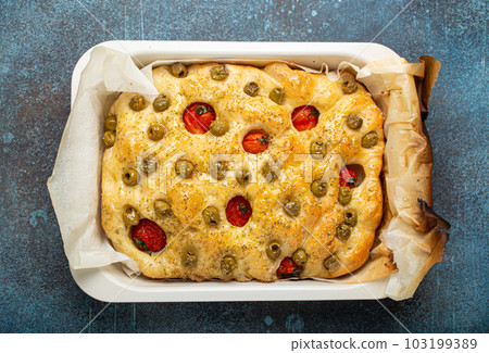 Overhead of Traditional Italian Homemade Flat Bread Focaccia with Green Olives, Olive Oil, Cherry Tomatoes and Rosemary in Baking Tray on Rustic Dark Blue Stone Background Overhead of Traditional Italian Homemade Flat Bread Focaccia with Green Olives, Olive Oil, Cherry Tomatoes and Rosemary in Baking Tray on Rustic Dark Blue Stone Background 103199389