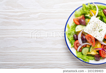 Traditional Greek Salad with Feta Cheese, Tomatoes, Bell Pepper, Cucumbers, Olives, Herbs in white ceramic bowl on White rustic wooden table background from above, Cuisine of Greece. Space for text Traditional Greek Salad with Feta Cheese, Tomatoes, Bell Pepper, Cucumbers, Olives, Herbs in white ceramic bowl on White rustic wooden table background from above, Cuisine of Greece. Space for text 103199403