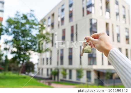 Hand holding keys on the background of a new building, construction concept. Buying real estate, housing, apartments. 103199542