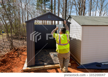 An individual assembles together plastic vinyl storage shed for his backyard An individual assembles together plastic vinyl storage shed for his backyard 103200047