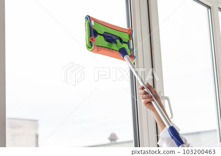 Happy woman cleaning window with sponge mop at home - housework and housekeeping concept 103200463