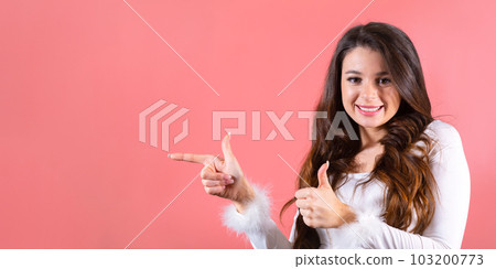 A pretty young woman gesturing with her fingers and showing on the copy space over pink background  103200773