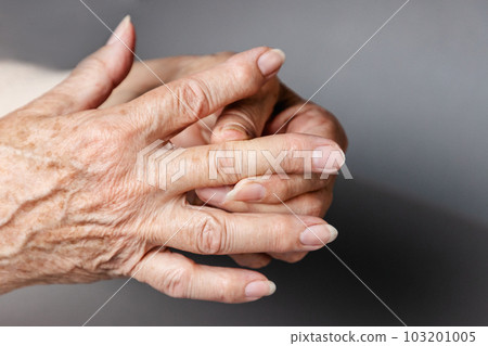 A senior woman massages her fingers, experiencing pain in the joints. Gray background, hands close-up. The concept of rheumatism and arthritis 103201005