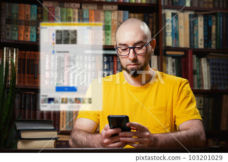 Social network. A bald man with glasses uses a smartphone. Digital clear window above the phone.There are shelves of books in the background.The concept of fake news, distance learning, and quarantine Social network. A bald man with glasses uses a smartphone. Digital clear window above the phone.There are shelves of books in the background.The concept of fake news, distance learning, and quarantine 103201029