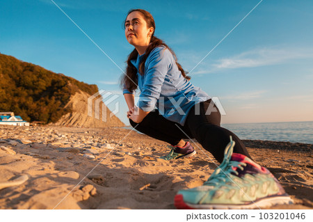 Young woman doing stretching on the sandy beach of the ocean. Outdoor. Sports and healthy lifestyle. Bottom view. Close-up sneakers Young woman doing stretching on the sandy beach of the ocean. Outdoor. Sports and healthy lifestyle. Bottom view. Close-up sneakers 103201046