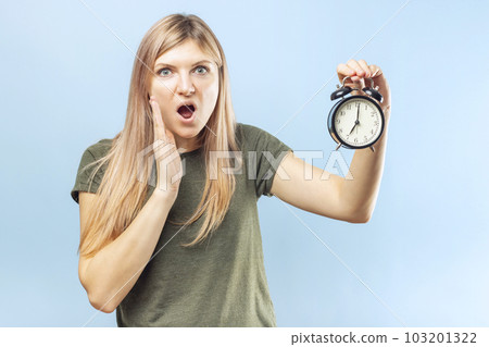 Young blonde woman with black alarm clock on blue background 103201322