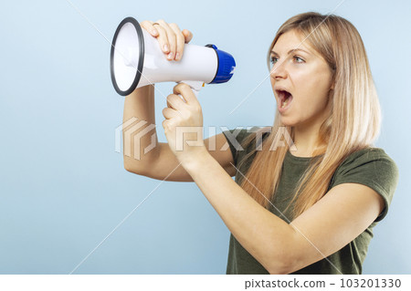 Young blonde woman shouting loudly while holding a megaphone on blue background 103201330