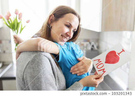 Boy congratulating his mom and giving her flowers tulips and greeting card 103201343