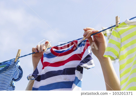 A woman hangs up kids clothes on a clothesline against the sky on a beautiful 103201371