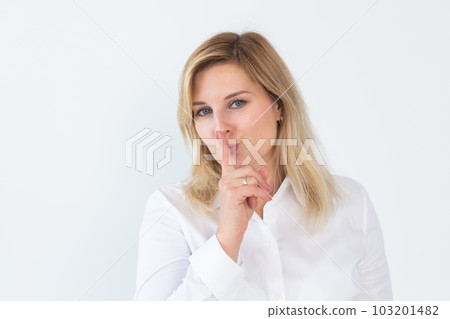 Beautiful young Caucasian woman isolated on white studio background hold finger at lips ask be silent quiet. Millennial female look at camera tell share mystery, announce secret sale or discount 103201482