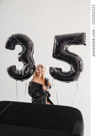 a naked blonde with tattoos in a black coat by a black sofa. birthday 103202322