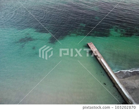 Aerial top down view of old concrete pier or breakwater with emerald sea water  103202870