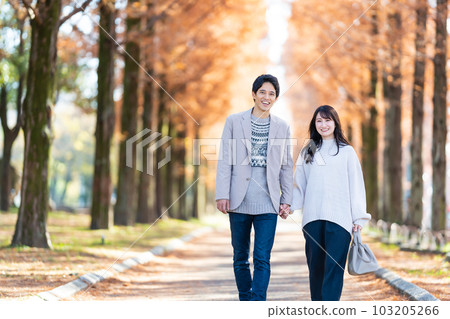 Young couple walking hand in hand along a tree-lined street 103205266