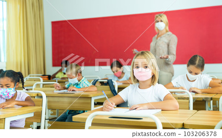Primary school students in protective masks sit at school desk in classroom Primary school students in protective masks sit at school desk in classroom 103206378