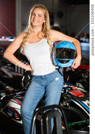 Smiling woman with helmet standing near cars for motor racing in sport club 103206408