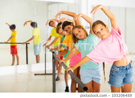 Preteen girls working near ballet barre during class 103206489