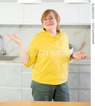 Cheerful senior woman standing in her kitchen smiling Cheerful senior woman standing in her kitchen smiling 103206679