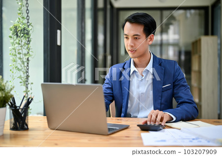 A handsome Asian businessman focuses on his work on laptop in his office. 103207909