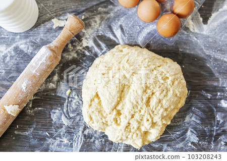 Top view of dough, rolling pin and baking ingredients on a dark wooden table 103208243
