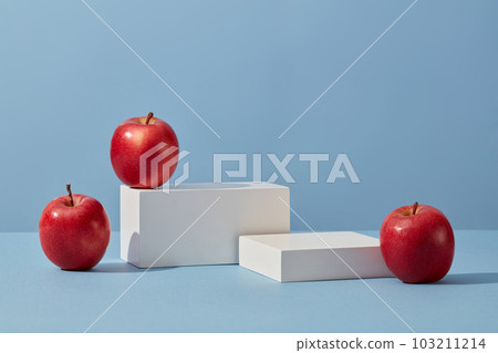 White podium in rectangle-shaped decorated with apples over a blue background. Apple (Malus domestica) helps to inhibit the increase of sebum secretion 103211214