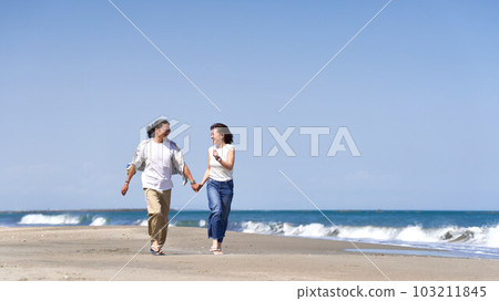 A middle-aged couple holding hands and running on the beach A middle-aged couple holding hands and running on the beach 103211845