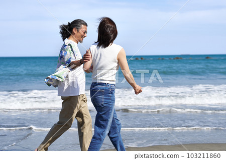 Middle-aged men and women walking on the beach with a smile Middle-aged men and women walking on the beach with a smile 103211860