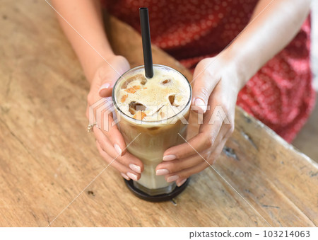 Woman's hands holding a glass of ice coffee Woman's hands holding a glass of ice coffee 103214063