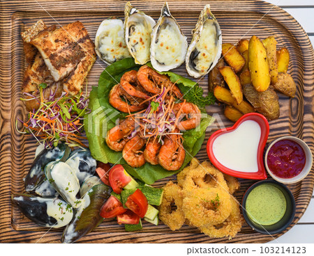A lot of seafood as fried fish, calamari, oysters and sauces on wooden board on the table A lot of seafood as fried fish, calamari, oysters and sauces on wooden board on the table 103214123