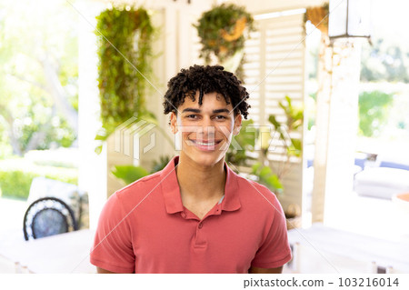 Portrait of biracial young man smiling and looking at camera while sitting at home, copy space 103216014