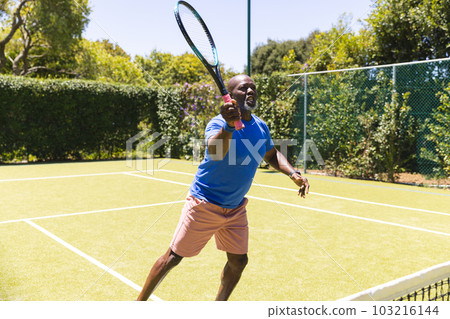 Happy senior african american man playing tennis on sunny grass court 103216144