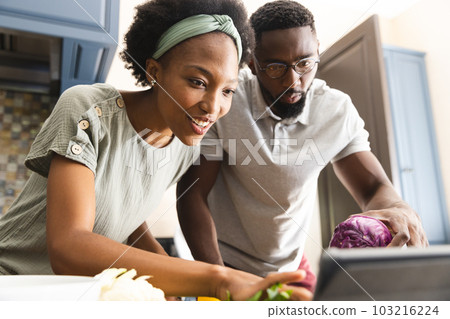 Happy african american couple preparing meal together using tablet in kitchen 103216224