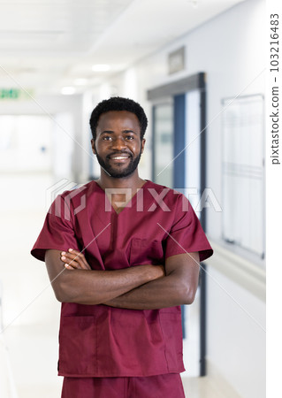 Unaltered portrait of african american male doctor in scrubs smiling, standing in hospital corridor Unaltered portrait of african american male doctor in scrubs smiling, standing in hospital corridor 103216483