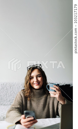 Young student taking a break from online studies, enjoying coffee and phone, laughing at memes and Young student taking a break from online studies, enjoying coffee and phone, laughing at memes and 103217179