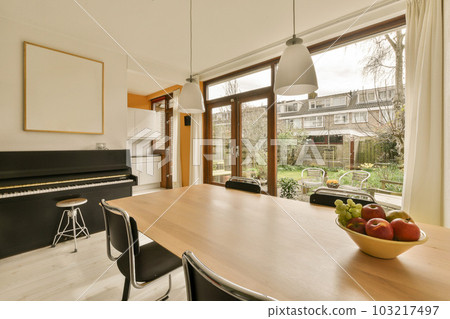 a dining room with a piano and fruit bowl on the table in front of an open patio door that leads to a garden 103217497