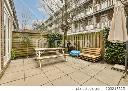 a backyard area with benches, tables and umbrellas on the patio in front of an apartment building that is surrounded by trees 103217525